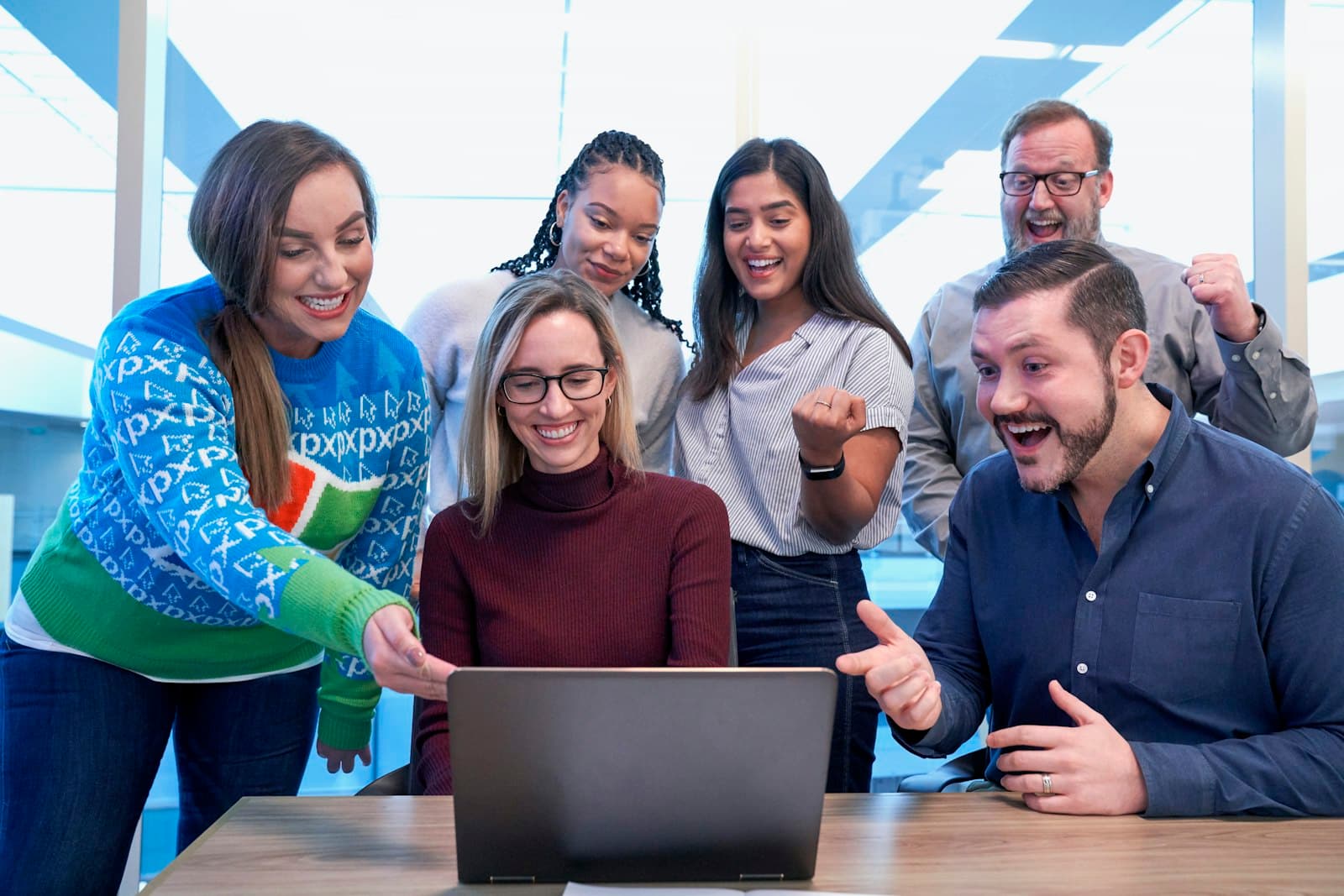 A group of colleagues cheering and laughing together around a laptop