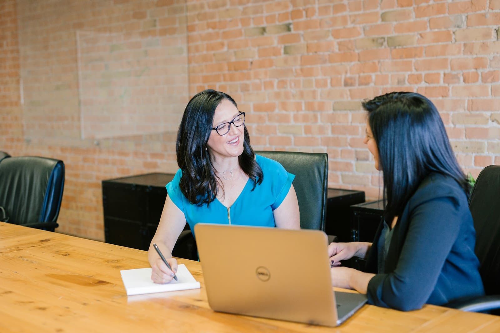 Two colleagues talking through notes at a table with a laptop